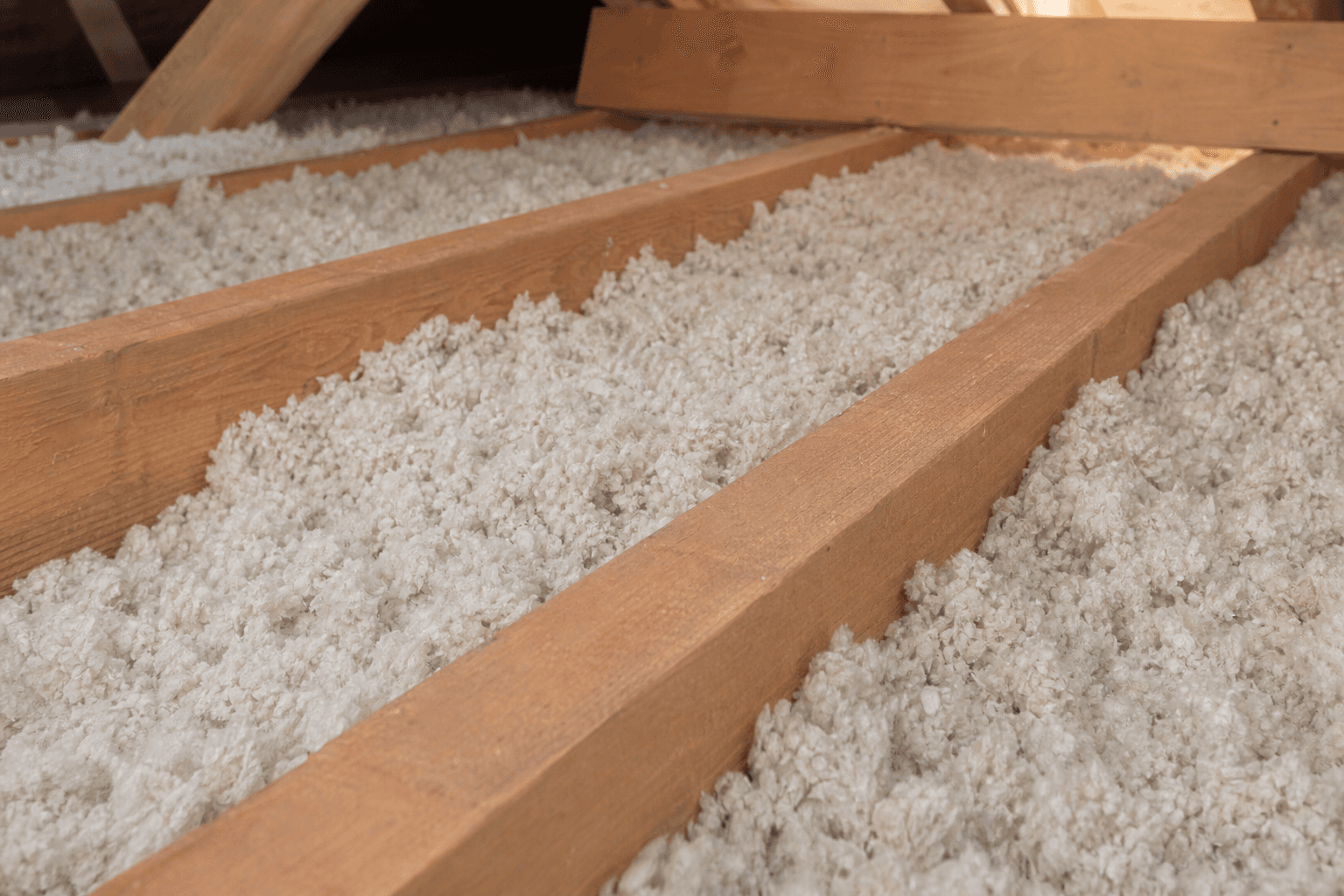 Détail de laine isolante soufflée entre solives de bois dans des combles perdus, texture homogène pour la performance thermique.